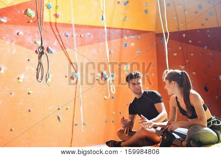 Common activity. Overjoyed young active couple sittiing in a climbing gym after training and climbing up the wall.