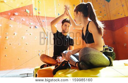 Cheerful gesture. Smiling young active couple giving high five while sittiing in a climbing gym after training.