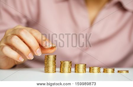 Savings female hand stacking gold coins into increasing columns
