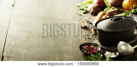 Cast iron pot and vegetables on wooden rustic table. Homemade food, cooking, vegetarian concept