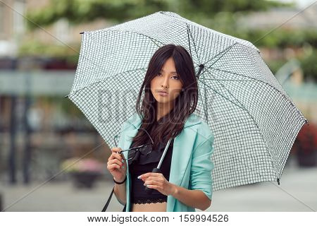 Confident asian girl city portrait. Serious woman outside with umbrella in casual business suite looking at camera. Beautiful young mixed race Asian Caucasian woman.