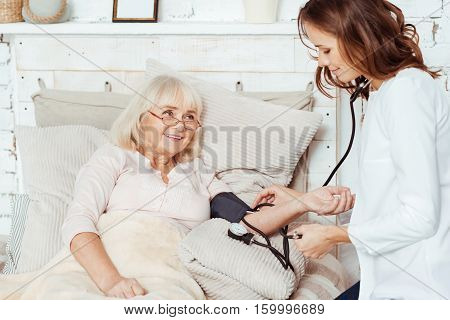 Good attitude. Pleasant professioanl nurse visiting pleasant elderly woman at home and measuring her blood pressure