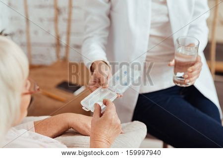 One pill for today. Pleasant caring professioanl nurse giving pills to elderly ill woman who is lying in bed and feeling sick at home