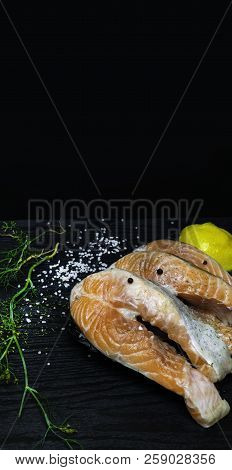 Slices Of Red Fish Salmon On Trout With Lemon, Dill, Pink And White Salt, On Black Wooden Background