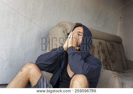 Depressed, Desperate Young Man Sitting On The Building Rooftop Terrace, Wearing Hoodie, Holding Head