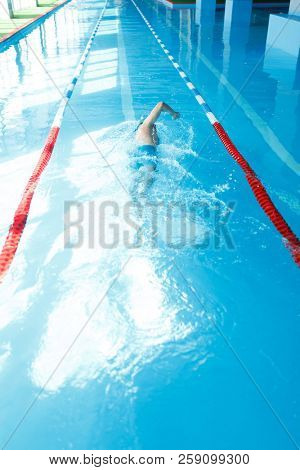 Image of young sporty man in blue cap swimming on back in swimming pool