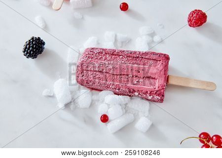 Berry apetitic organic ice cream lolly is represented on a gray marble table with different berries and ice cubes with a copy of the space