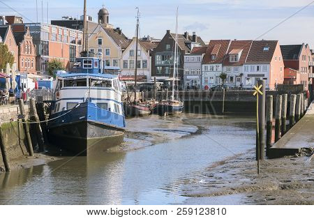 Inner Harbor At Low Tide In The Old Town Of Husum With Boats On The Mudflat And Houses On A Sunny Da