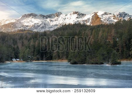 Winter Landscape With A Frozen Lake Surrounded By Green Fir Forest And The Snowy Peaks Of The Alps M