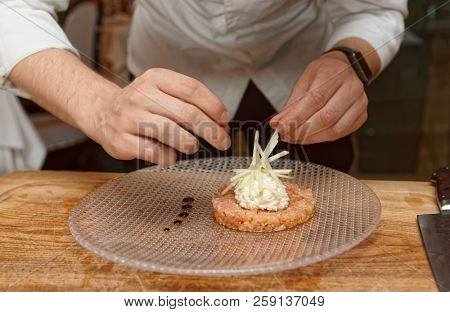 Chef is decorating salmon tartar with cut apple and whipped cheese cream