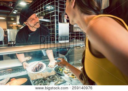 Experienced chef choosing raw seafood from the freezer for two customers in a trendy restaurant or cafeteria with fresh food