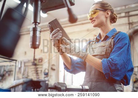 Woman in metal workshop checking workpiece for accuracy 