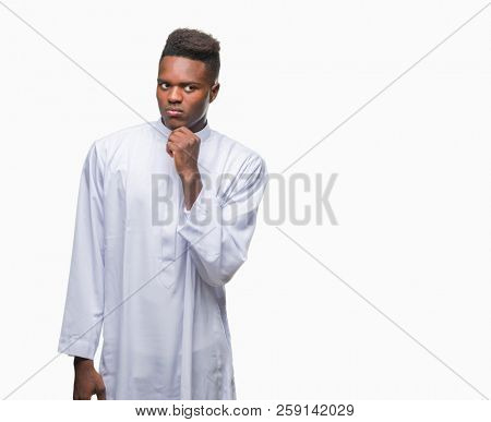 Young arabic african man wearing traditional djellaba over isolated background with hand on chin thinking about question, pensive expression. Smiling with thoughtful face. Doubt concept.