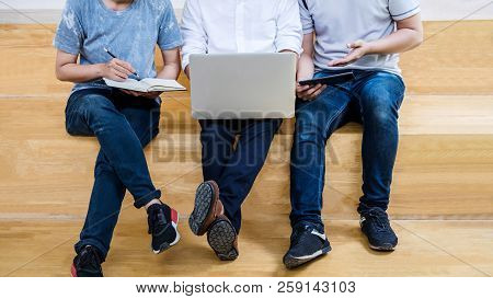 High School Tutor Or College Student Group Sitting At Desk In Library Studying And Reading, Doing Ho