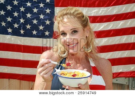 una donna si gode una ciotola di cereali con latte e lamponi una mattina davanti alla sua bandiera americana