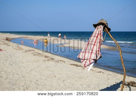 Camouflage Hat And Plaid Shirt On A Pole Against The Backdrop Of A Seaboard And The Blue Sea