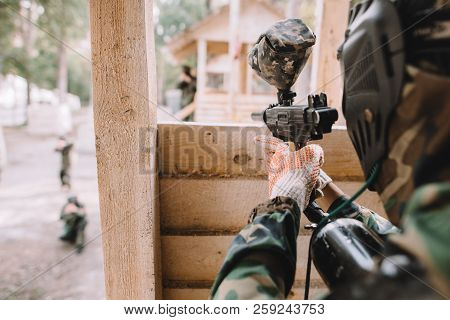 Selective Focus Of Paintball Player In Camouflage Uniform Aiming By Paintball Gun From Wooden Tower 