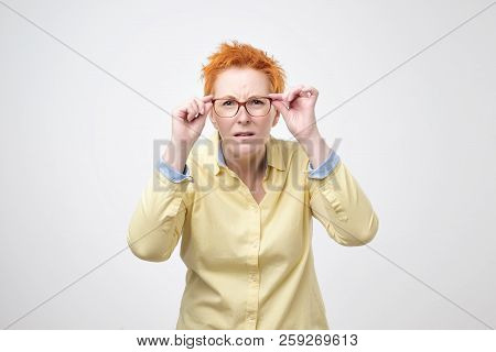 Attentive Caucasian Woman With Short Red Hair Looks Scrupulously Into Distance, Keeps Hand On Rim Of