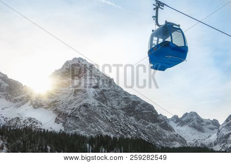 Single Cable Car Traveling In The Alps Mountains Covered By Snow, While The December Sun Shines On T