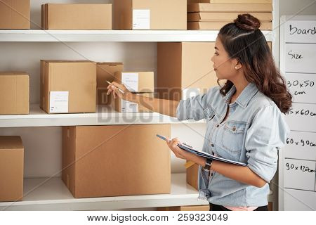 Asian Postwoman Checking Parcels On The Shelves At Post Office