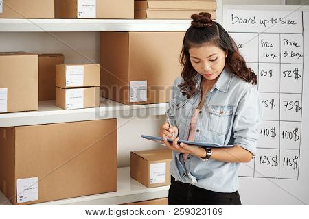 Asian Young Postwoman Checking Parcels On Her Checklist At Warehouse