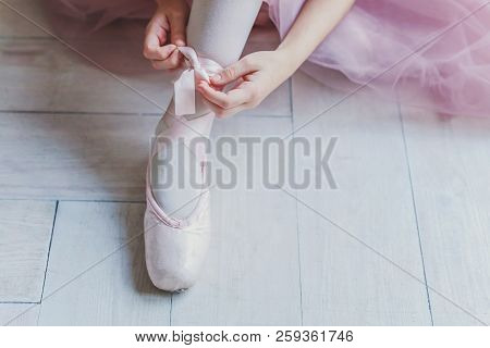 Hands Of Ballerina In Pink Tutu Skirt Puts On Pointe Shoes On Leg In White Light Hall. Young Classic