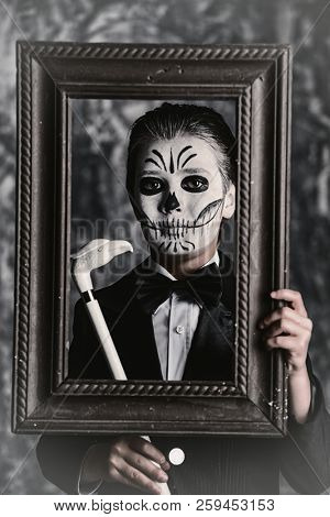 Portrait of a child boy with carnival make-up of a skeleton wearing elegant tail-coat. Studio shot over dark grunge background. Halloween. Dia de los muertos. The Day of the Dead.