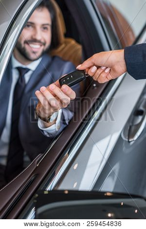 Partial View Of Female Seller Giving Car Key To Smiling Businessman In New Car At Dealership Salon