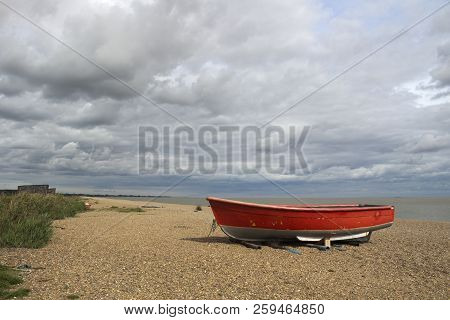 Red Fishing Boat On Dunwich Beach, Suffolk, England On A Cloudy Day