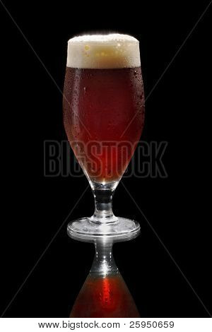 Donker bier in een footed glas op reflecterend oppervlak.