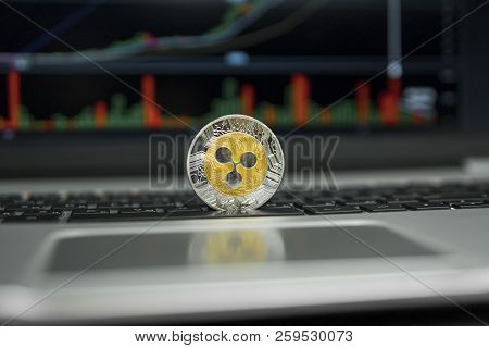 Golden And Silver Ripple Coin On A Black Keyboard Of Silver Laptop And Diagram Chart Graph On A Scre
