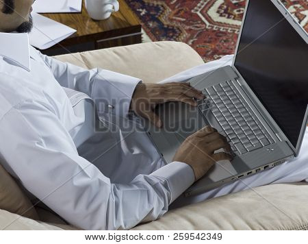 Mideastern Man Using Laptop At Office, With A Cup Of Cofee And Documents On The Side Table
