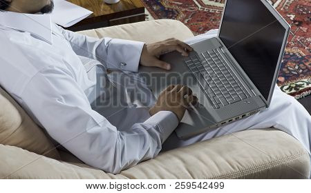 Mideastern Man Using Laptop At Office, With A Cup Of Cofee And Documents On The Side Table