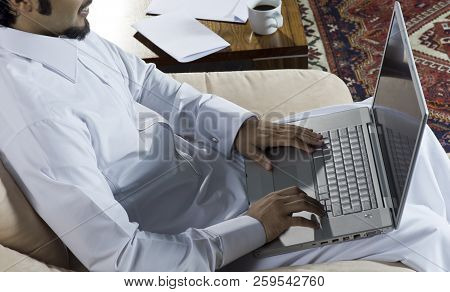 Mideastern Man Using Laptop At Office, With A Cup Of Cofee And Documents On The Side Table