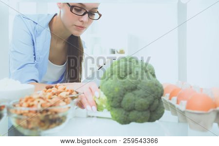 Portrait Of Female Standing Near Open Fridge Full Of Healthy Food, Vegetables And Fruits. Portrait O