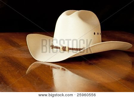 Hvid stråhat i cowboy med et hattebånd på et træbord mørk baggrund