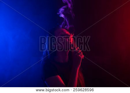 Young Woman Smoking Vape Or E-cigarette In Neon Light