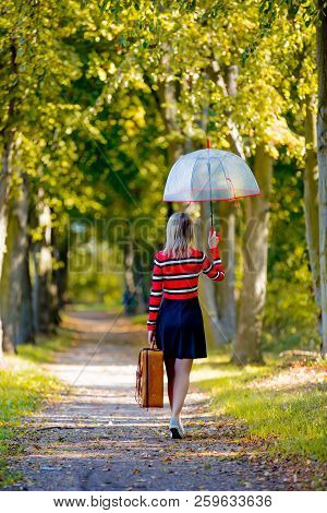 Young Girl With Umbrella And Suitcase In Park In Autumn Season