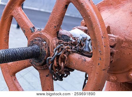 Old Rusty Weather-beaten Round Valve Part Of The Heat System With A Long Bolt With Chain Rings Indus