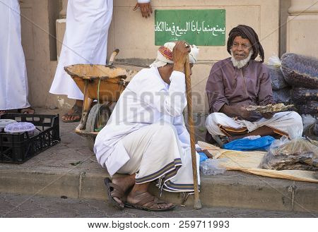 Nizwa, Oman, 21 September 2018: Omani Man Selling Dry Fish And Dates At A Friday Market, Sign In Ara