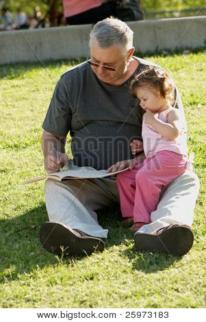 The grandfather with grand daughter sitting on a grass in park