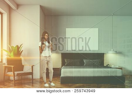 Woman Looking At Smartphone Screen In White Minimalistic Bedroom Interior With Wooden Floor, Masterb