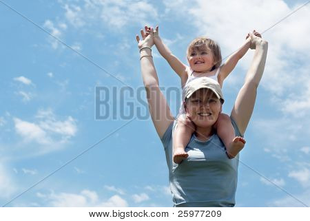 A mãe com uma filha pequena contra o céu