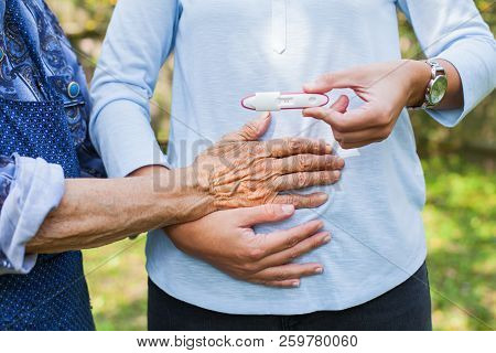 Close Up Picture Of Young Woman Holding Pregnancy Test With Grandmother. Great-grandchild On The Way