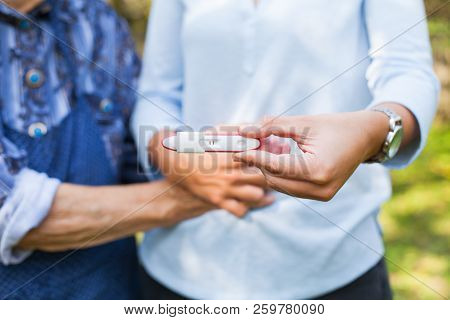 Close Up Picture Of Young Woman Holding Pregnancy Test With Grandmother. Great-grandchild On The Way