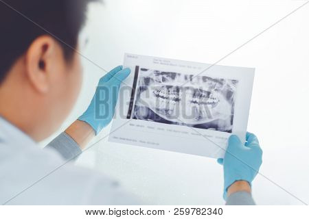 Dentist Consulting With Patient Presenting Results On Dental X-ray Film About The Problem Of The Pat