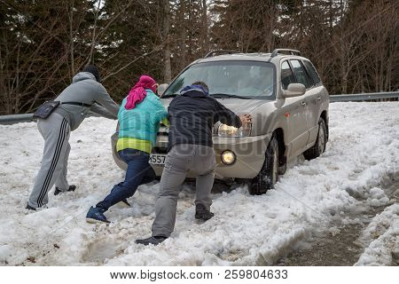 Adygea, Russia, 05 May 2015: Three People Push A Car That Is Stuck In Deep Snow