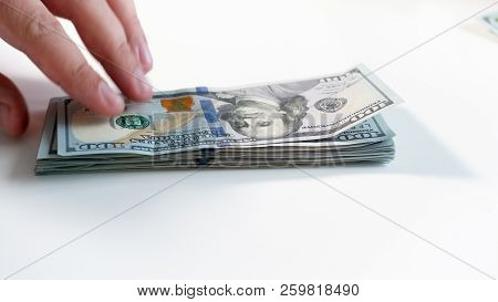 Closeup Image Of Hand Taking Stack Of Dollars Lying On Hwite Wooden Desk