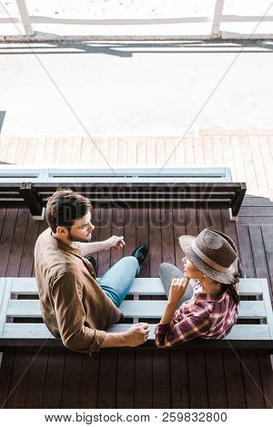 High Angle View Of Cowboy And Cowgirl Sitting On Bench At Ranch Stadium And Looking At Each Other