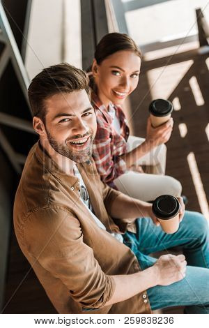 High Angle View Of Smiling Man And Woman Sitting With Coffee To Go At Ranch And Looking At Camera